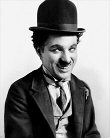 A smiling man with a small moustache wearing a bowler hat and a tight-fitting necktie and coat.