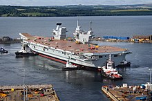 A Queen Elizabeth-class aircraft carrier docked in Scotland. This ship is one of two aircraft carriers, Portsmouth is its home port.