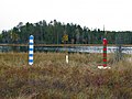 Finland–Russia border markers: a white marker for the actual border, "guarded" by striped bollards, marked with a coat of arms, maintained by each state.