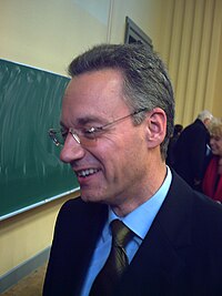 A middle-aged man in glasses and a suit, looking to the left
