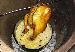A whole chicken suspended above rice and charcoal.