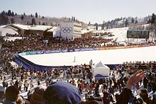 Photographie de l'aire d'arrivée d'une piste de ski entourée de gradins remplis par la foule.