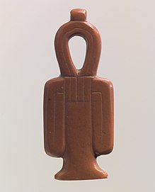 A red stone amulet shaped like a column with a looped top and two loops hanging at the sides