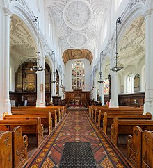 The interior of a church, facing down the aisle towards the altar. The ceiling is white and intricately patterned like lace.