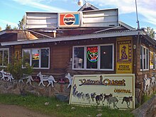 A wooden building is decorated with signs and the carved outline of a dog team