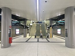 Tiled underground platform with escalators and stairs in the middle