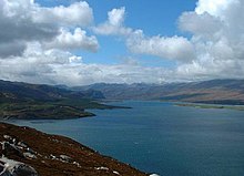 Colour photograph of a body of water surrounded by hills viewed from a hill