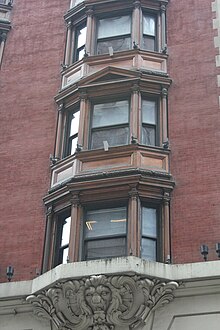 Detail of one bay of windows on the third through fifth stories. On each story is an oriel window, which is angled outward. The facade is made of brick.