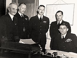 Five men, four standing and one seated, wearing dark-coloured military uniforms