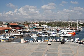 Port of Paphos on the lower half of the picture, with boats docked on it, and on the upper half, a view of the city of Paphos