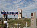 Border stone in China, foreground right, with Russian border marker to its left in background, striped red and green. The large gate is entirely in Russian territory.