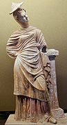 Jeune femme drapée appuyée contre un pilier, production de Tanagra, fin IIIe siècle av. J.-C. ou début IIe siècle av. J.-C. Musée du Louvre.