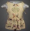A loose vest-like garment in a faded cream color with bright red and green embroidery depicting plants and birds.