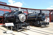 Two small steam locomotives parked in front of a locomotive roundhouse. The left locomotive reads "New Haven Trap Rock Co." and is numbered 43. The right locomotive reads "E. J. Lavino and Co."