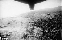 Black and white aerial photograph of an airfield in a jungle clearing. Part of the fuselage of the aircraft is visible at the top of the photograph.