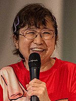 Mayumi Tanaka holding a microphone and smiling