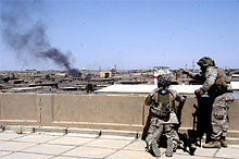 Two Marines on a rooftop observe billowing smoke from an Iraqi city.