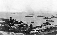 A group of large warships steaming slowly away from the city.