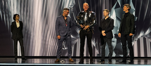 On stage, Timothée Chalamet stands to the left while four game developers accept an award at right, one dressed in armor.