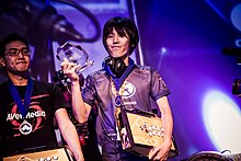 Momochi holding his Evo 2015 trophy and arcade stick; GamerBee shown on the side.