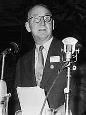 Man in a suit speaks at a microphone.