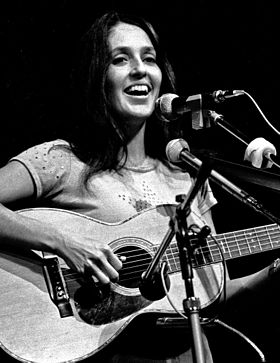 Baez at microphone, playing guitar, in sleeveless top