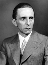 Foto hitam dan putih seorang pria yang mengenakan jas dan dasi. Tubuhnya menghadap ke kiri sementara kepalanya menghadap ke kanan.