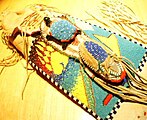 A Northern Ute Beaded Pipebag. This pipebag— made from brain-tanned mule-deer hide, glass trade beads, and eagle bone—incorporates the sacred symbols of the Ute: the blue fire, the yellow fire, the green of the earth, and the hail of the thunder beings; motifs of the turtle (earth) and moccasin (home), and the symbol of the red fire and the bear, sacred animal of the Ute.
