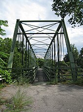 An image of the green Whipple truss bridge from along the side of a road