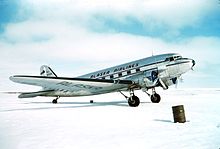 Right side view of a silver Douglas DC-3 aircraft parked on snow-covered ground