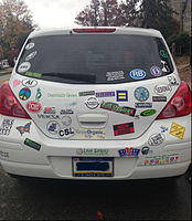 The rear of a Nissan Versa displaying many bumper stickers.