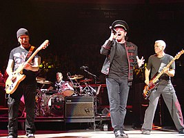 U2 performing at Madison Square Garden in November 2005, from left to right: The Edge; Larry Mullen, Jr. (drumming), Bono, and Adam Clayton