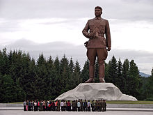 A crowd looking at a large statue depicting young Kim Il Sung in military attire
