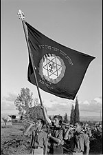 Members of Hashomer Hatzair in Kfar Saba branch blowing the trumpet as they wave the movement´s flag, 1941.