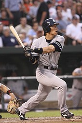 A man in a grey baseball uniform and blue batting helmet looks to the right as he clenches a swung baseball bat behind him.