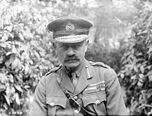 Julian Byng in a black and white chest high portrait with foliage behind him. Byng has a moustache and is wearing a general officer's uniform that consists of a tailored jacket adorned with brass buttons. The collar is embellished with additional decorations denoting rank and service branch. He is wearing a peaked cap featuring ornate insignia indicating his rank and unit affiliation.