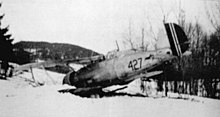 A black-and-white photo of a biplane sitting on the ground, shown in semi profile, viewed from the left-rear. The left wing and nose is buried in the ground.