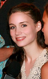 A brunette woman smiles at the camera as she looks slightly to her left
