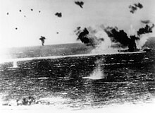 A large ship is surrounded by explosions in the air and water.