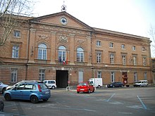 Photo couleur d'une façade en brique rouge de style néo-classique. Un fronton central porte une horloge.