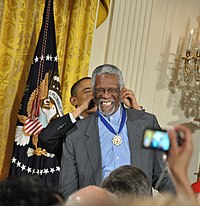 Russell smiling as Barack Obama puts an award around his neck