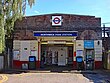 A brown-bricked building with a rectangular, dark blue sign reading "NORTHWICK PARK STATION" in white letters all under a light blue sky