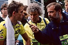 LeMond standing on the left of the picture in his racing jersey, being interviewed by a reporter