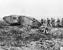 In the monochrome photograph, soldiers traverse the battlefield, walking alongside and behind a Mark II tank proudly displaying the number 598 on its side. In the foreground, there are the remains of a fallen soldier, adorned in British equipment, including a helmet.