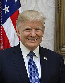 Potret resmi kepresidenan Gedung Putih. Potret kepala Trump tersenyum di depan bendera Amerika Serikat, mengenakan jas biru tua dengan pin kerah bendera Amerika, kemeja putih, dan dasi biru muda.