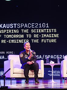 Photo of astronaut Dr. Sian Proctor holding a microphone and talking on stage during the space camp Space 2101 at the King Abdullah University of Science and Technology.