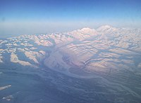 Aerial photo of the Denali and the snowy Alaska Range with a glacier leading to a river
