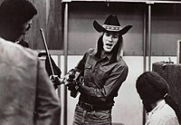 Photograph of Sahm holding a fiddle and bow talking to a man in a recording studio