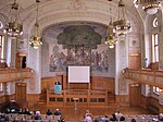 Göteborgs universitets aula (huvudbyggnaden). Föreläsningsrummet domineras av Nils Asplunds nationalromantiska väggmålning från 1907.