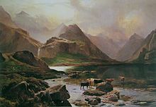 Tall, rocky mountains tower over a small lake, beyond which a waterfall cascades down from the heights. Brown and black cattle stand by the margins of the lake, lit by wan sunlight that streams through the clouds.